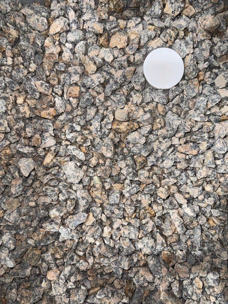 Top-down mobile photo of crushed aggregate with a white scale reference disc